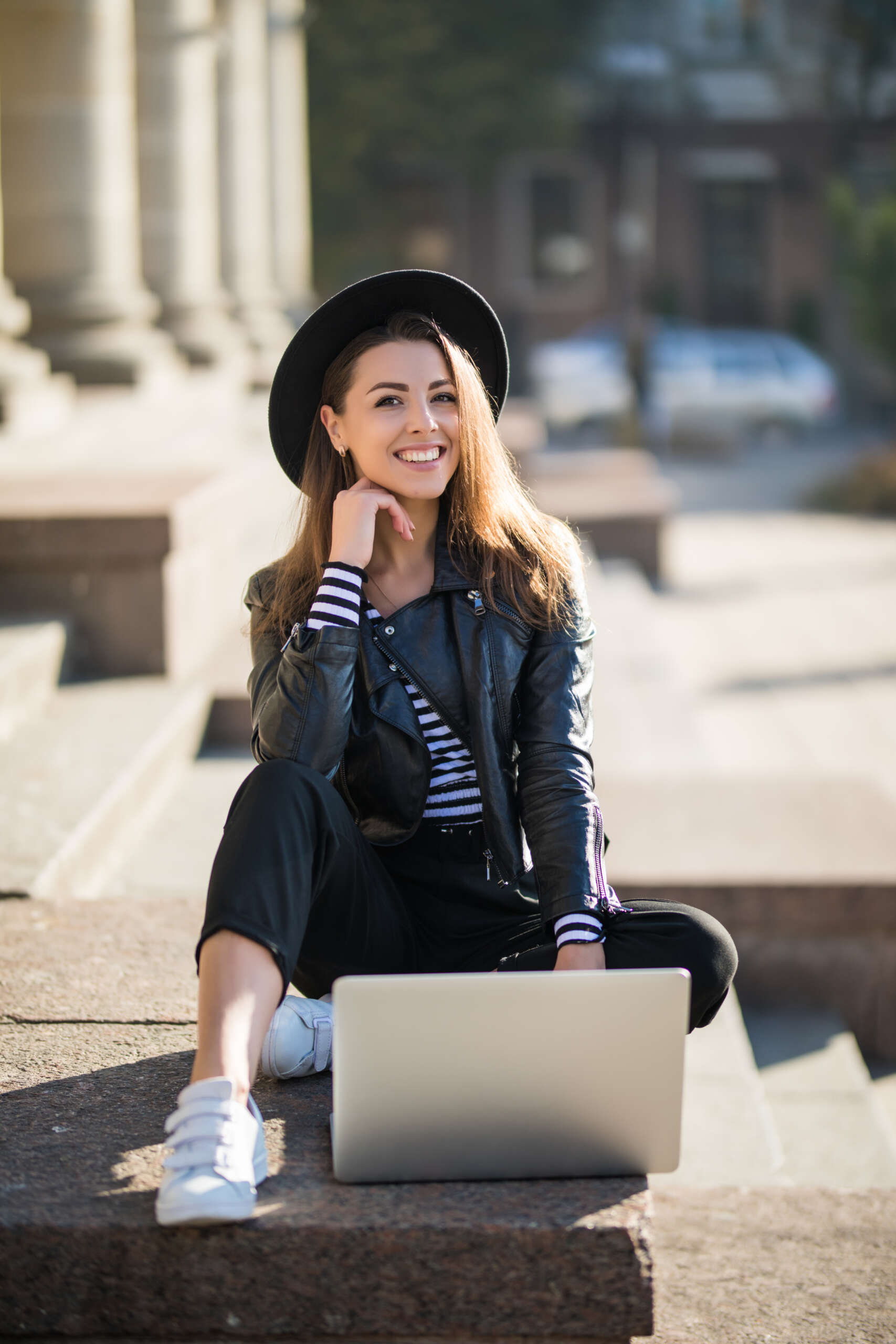 beautiful young businesswoman student girl works with her brand computer in the city centre sitting on the stone stairs in sunny day